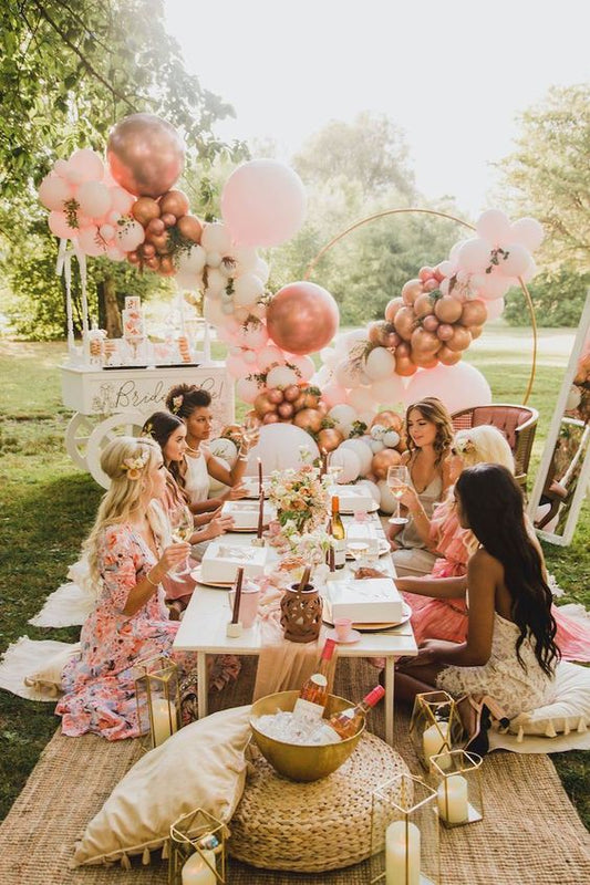 bridal shower picnic with girls in green garden with pink balloons and boho pillows